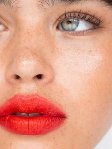 Close-up of a woman's face showing her eye, nose, and bright red lips. Hair and makeup by Amber Rose.