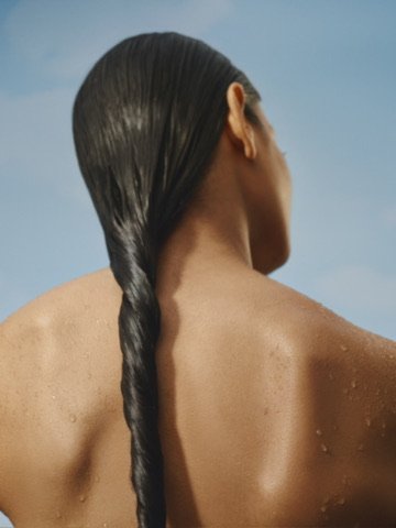 Back of a woman with wet hair braided, viewed from behind, against a sky background