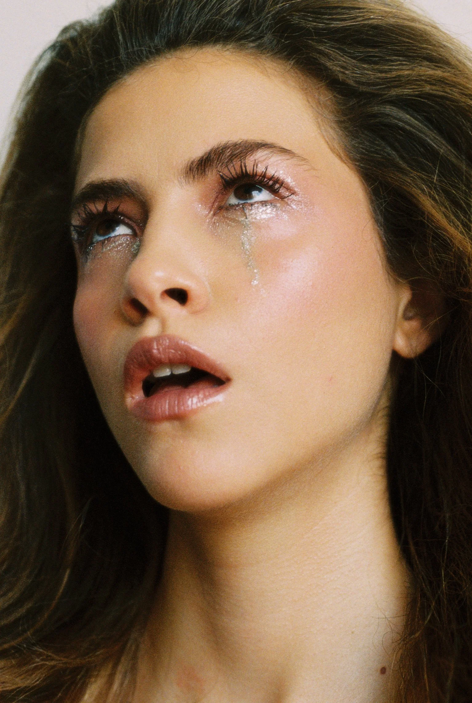 Close-up of a woman with long, brown hair and makeup, looking upward with tears on her face. Hair and makeup by Amber Rose.