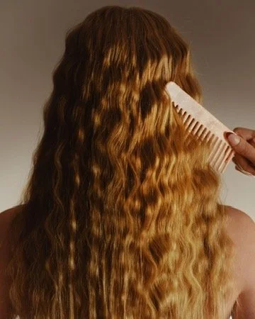 Person brushing long, wavy, red hair. Hair and makeup by Amber Rose.
