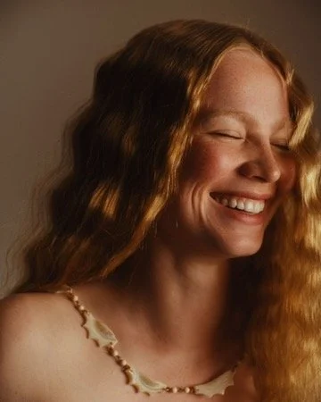 A woman with long, wavy red hair smiling with her eyes closed. Hair and makeup by Amber Rose.