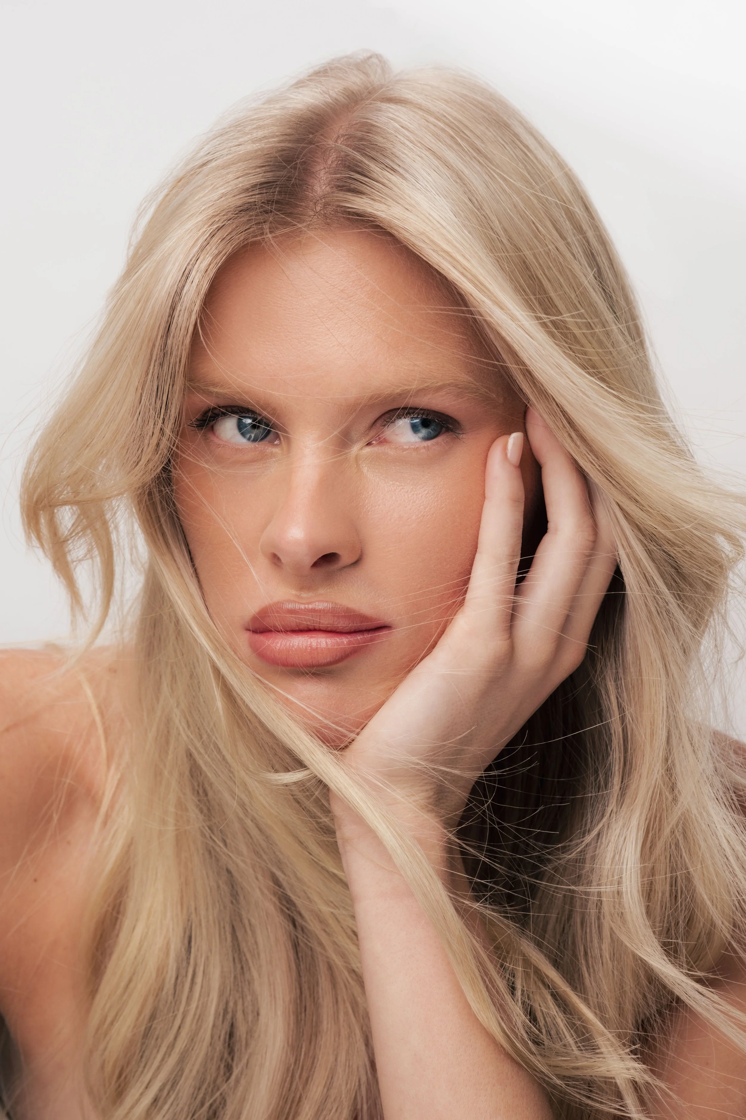 Natural beauty portrait of a blonde model resting her face in her hand, soft dewy makeup by Los Angeles commercial artist Amber Rose.