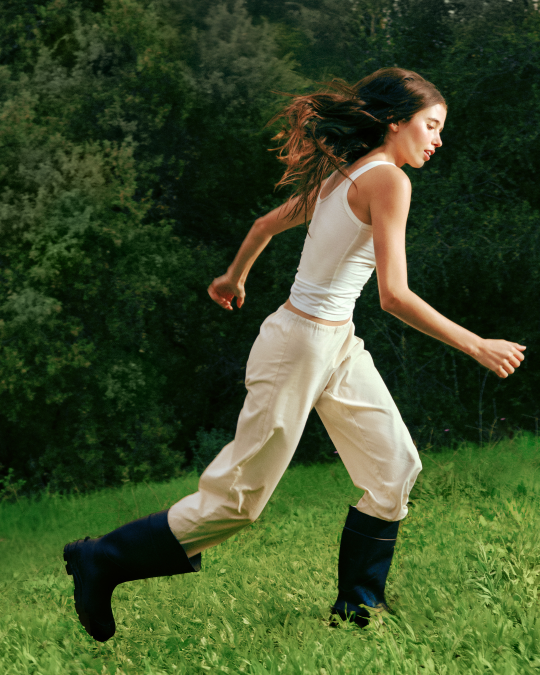 A woman running outdoors on a grassy field with green trees in the background.