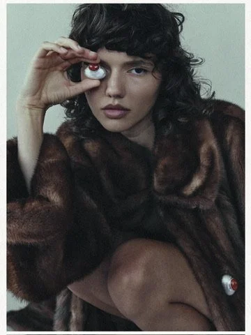 Playful editorial shot of a model in a plush fur coat holding a statement ring up to her eye, styled by Los Angeles hair and makeup artist Amber Rose.