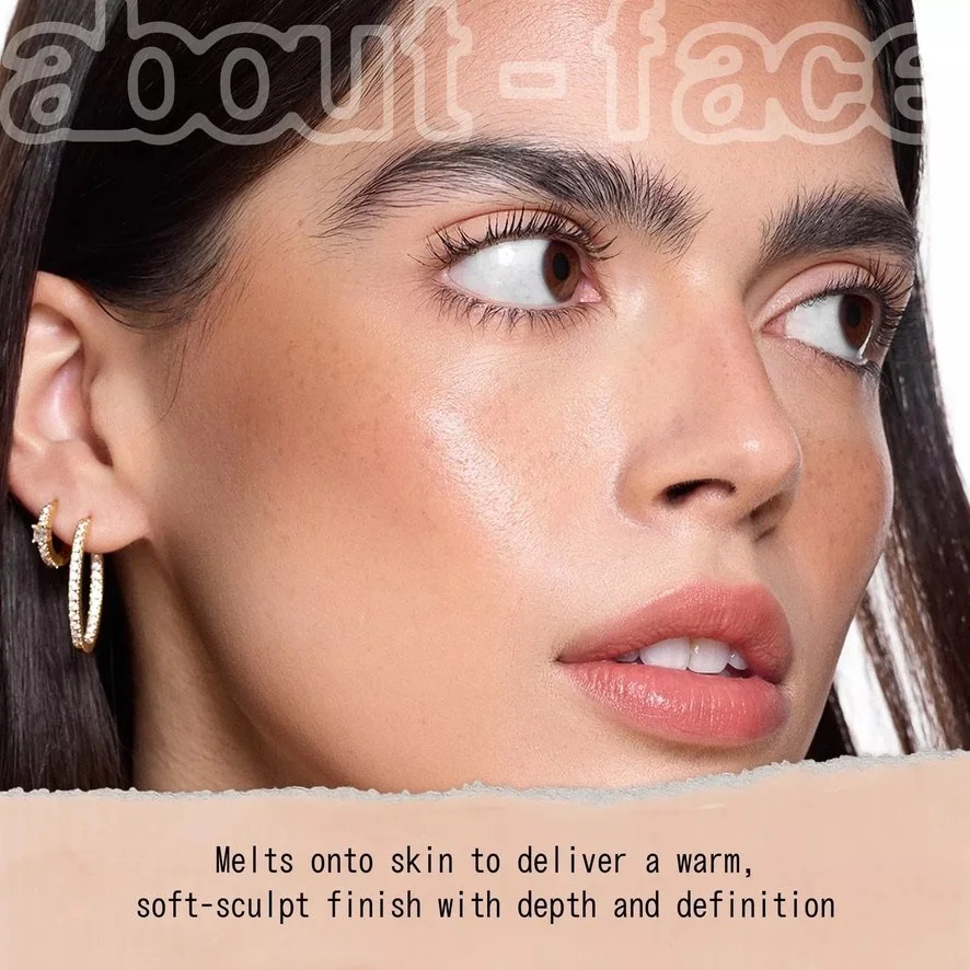 Close-up of a woman's face with smooth skin, brown eyes, and dark hair, wearing gold hoop earrings, with text overlaid describing makeup product features. Hair and makeup by Amber Rose.