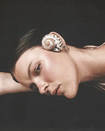 Reclining beauty portrait featuring a spiral seashell-style earring, editorial jewelry styling by Los Angeles hair and makeup artist Amber Rose.