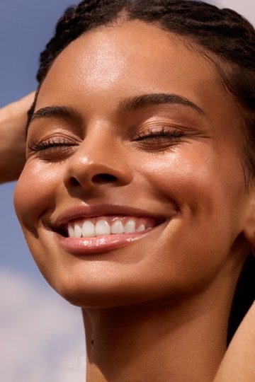 Close-up of a woman smiling with closed eyes, outdoors on a sunny day. Hair and makeup by Amber Rose.