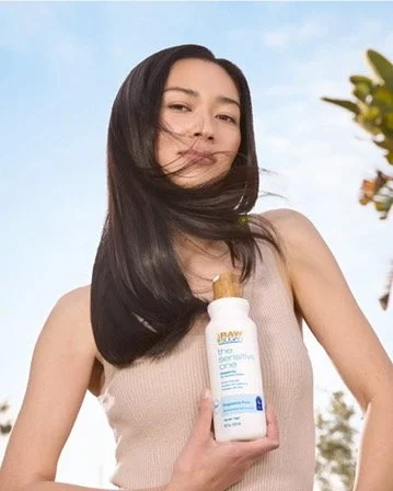 Young woman outdoors holding a bottle of skincare product with wind blowing her hair.
