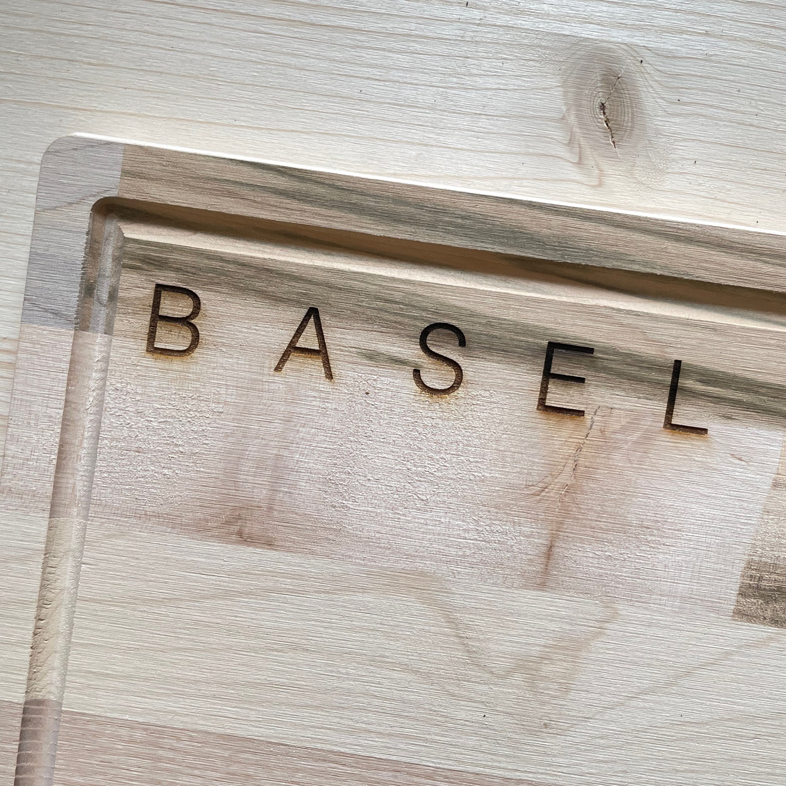 engraved beechwood cutting board with basel skyline and BASEL. Close up of word BASEL.