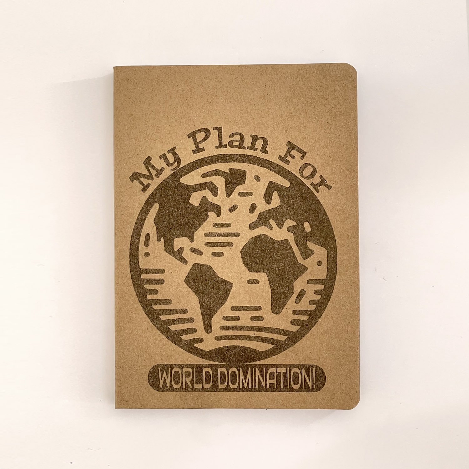 My Plan for World Domination" engraved on a kraft notebook with a globe design