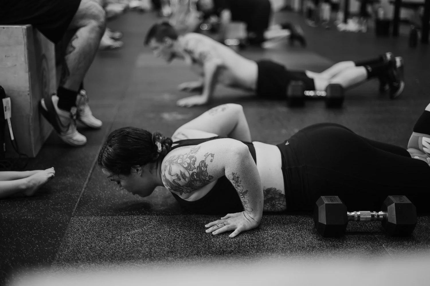 Female athlete completing a burpee at CrossFit TARIS in Brisbane, with other members visible in the background also doing the workout.