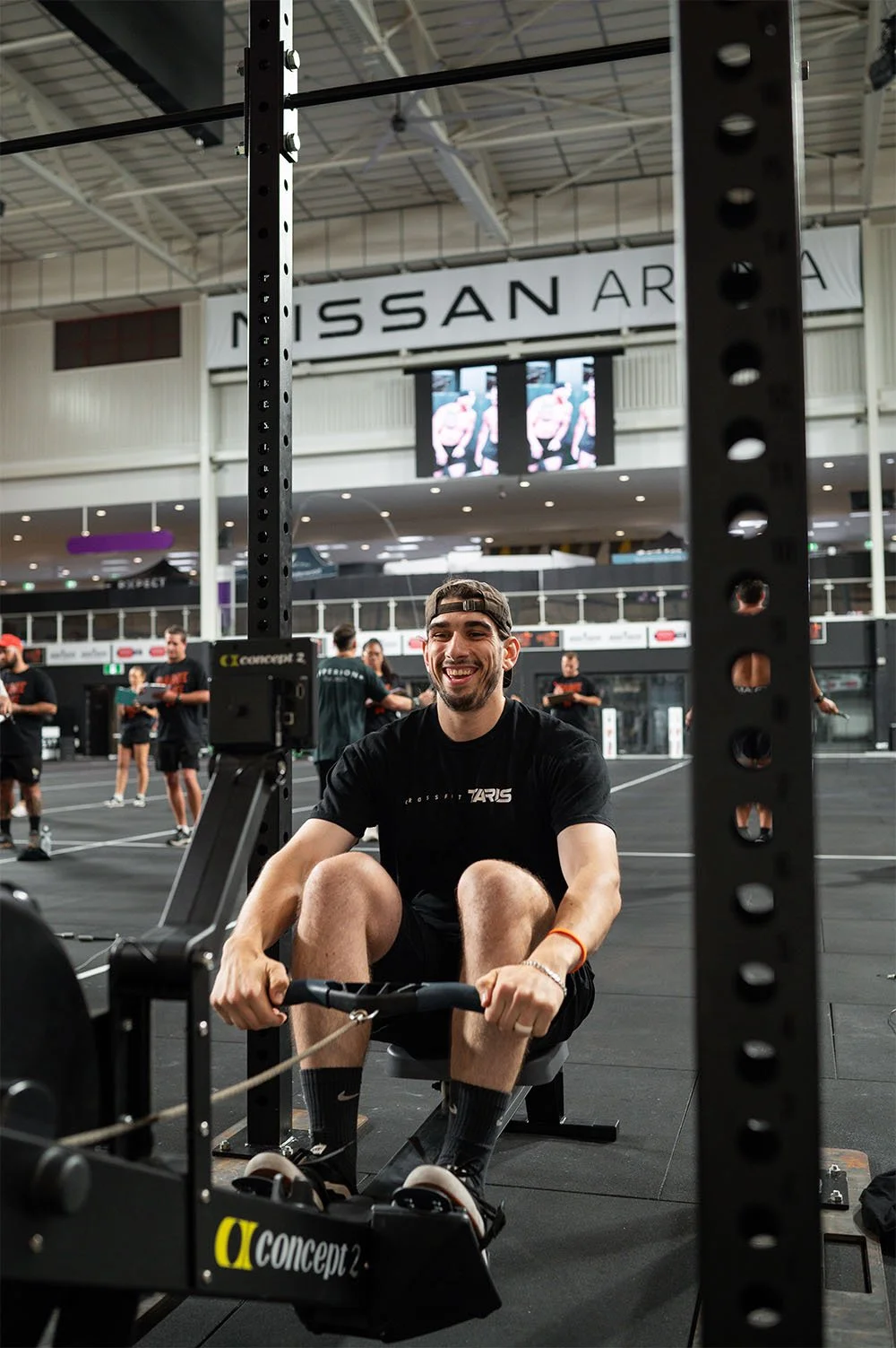 A male member of CrossFit TARIS competing in a local competition, using a rowing machine during a workout and smiling for the camera.