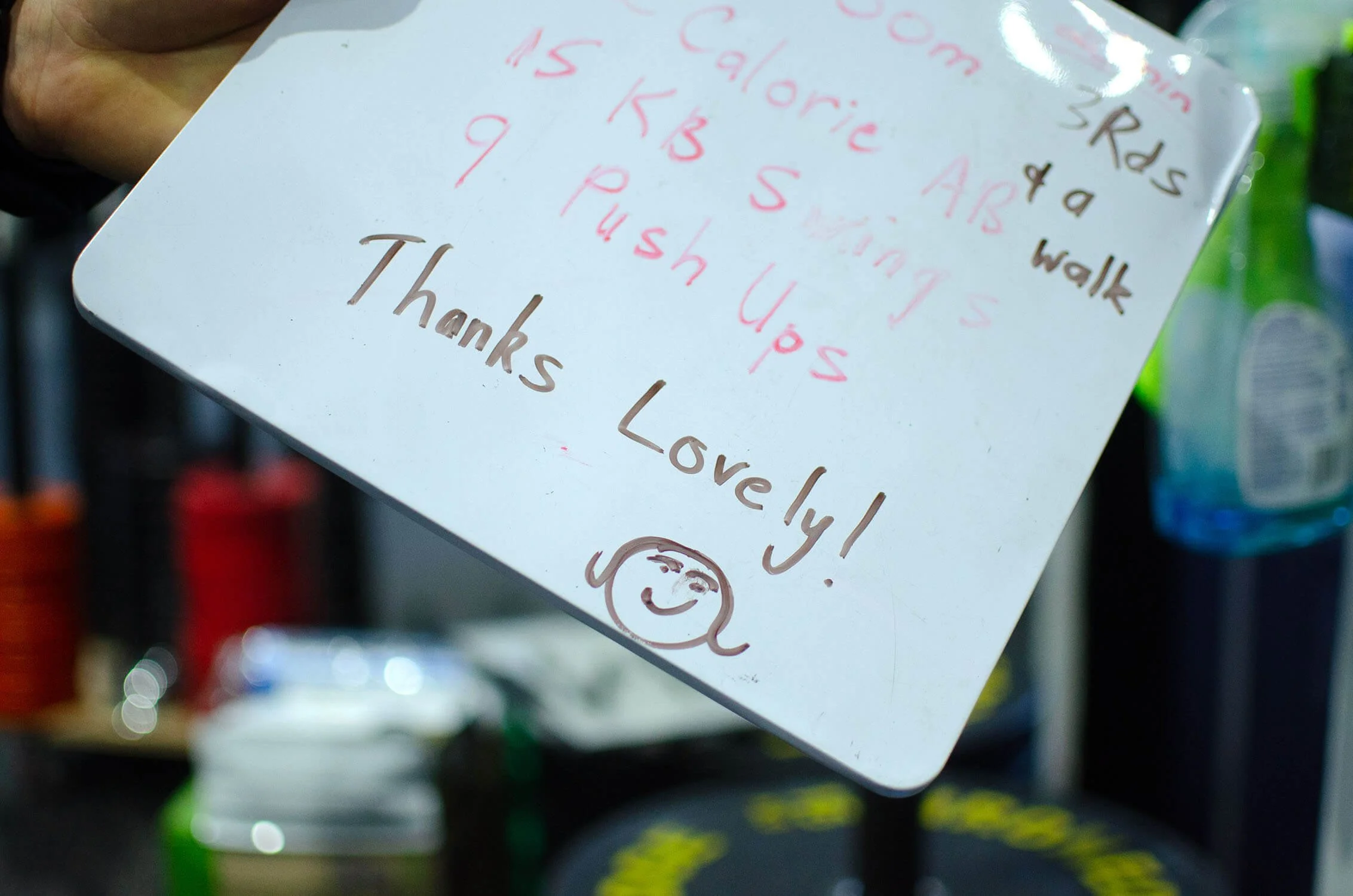A small whiteboard with a workout written on it, as well as a message for Coach Lisa Lake written down the bottom that reads 'Thanks lovely' with a smiley face underneath.