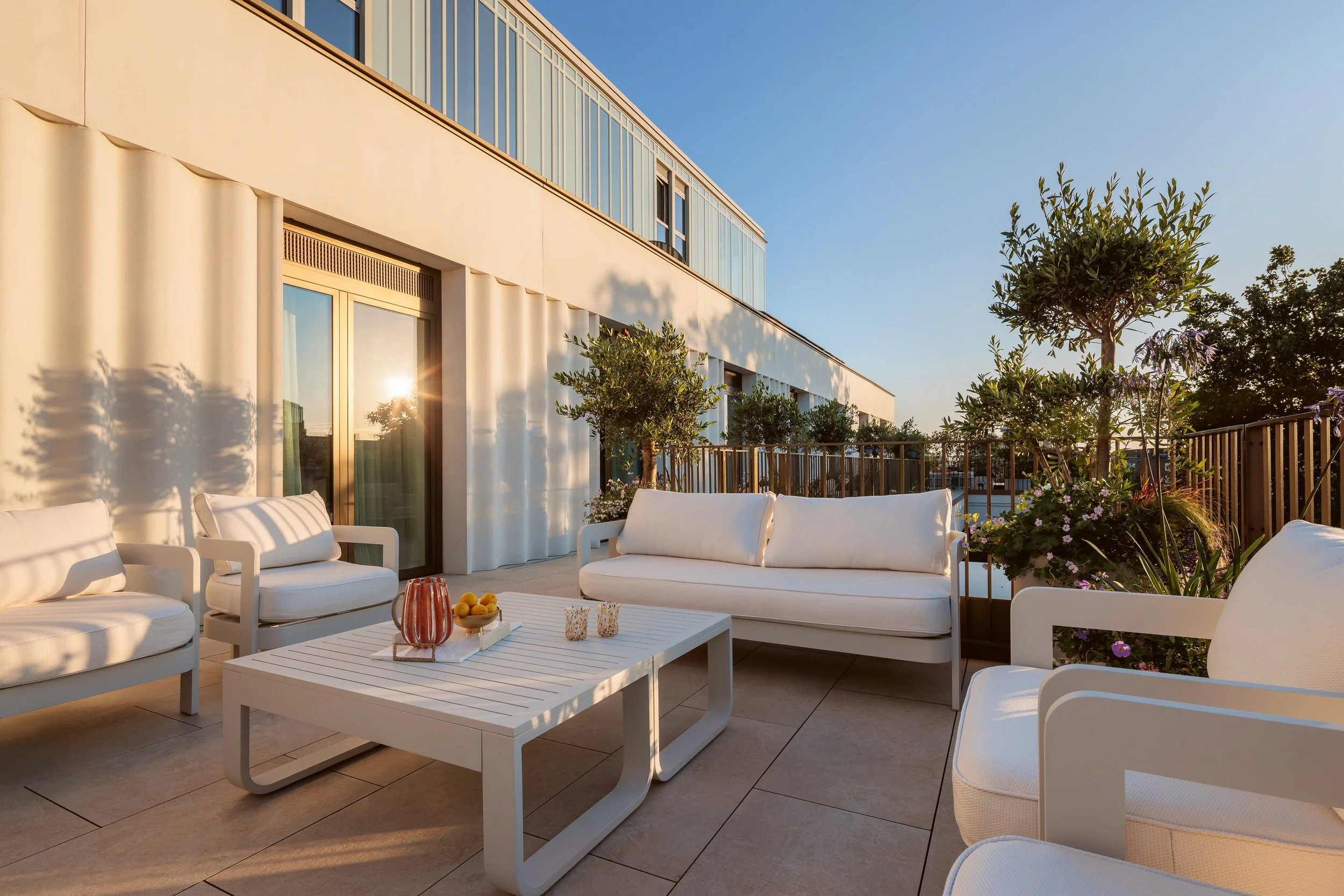 Sunlit private terrace with lounge seating and olive trees in a four-bedroom apartment at Holland Park Gate, London