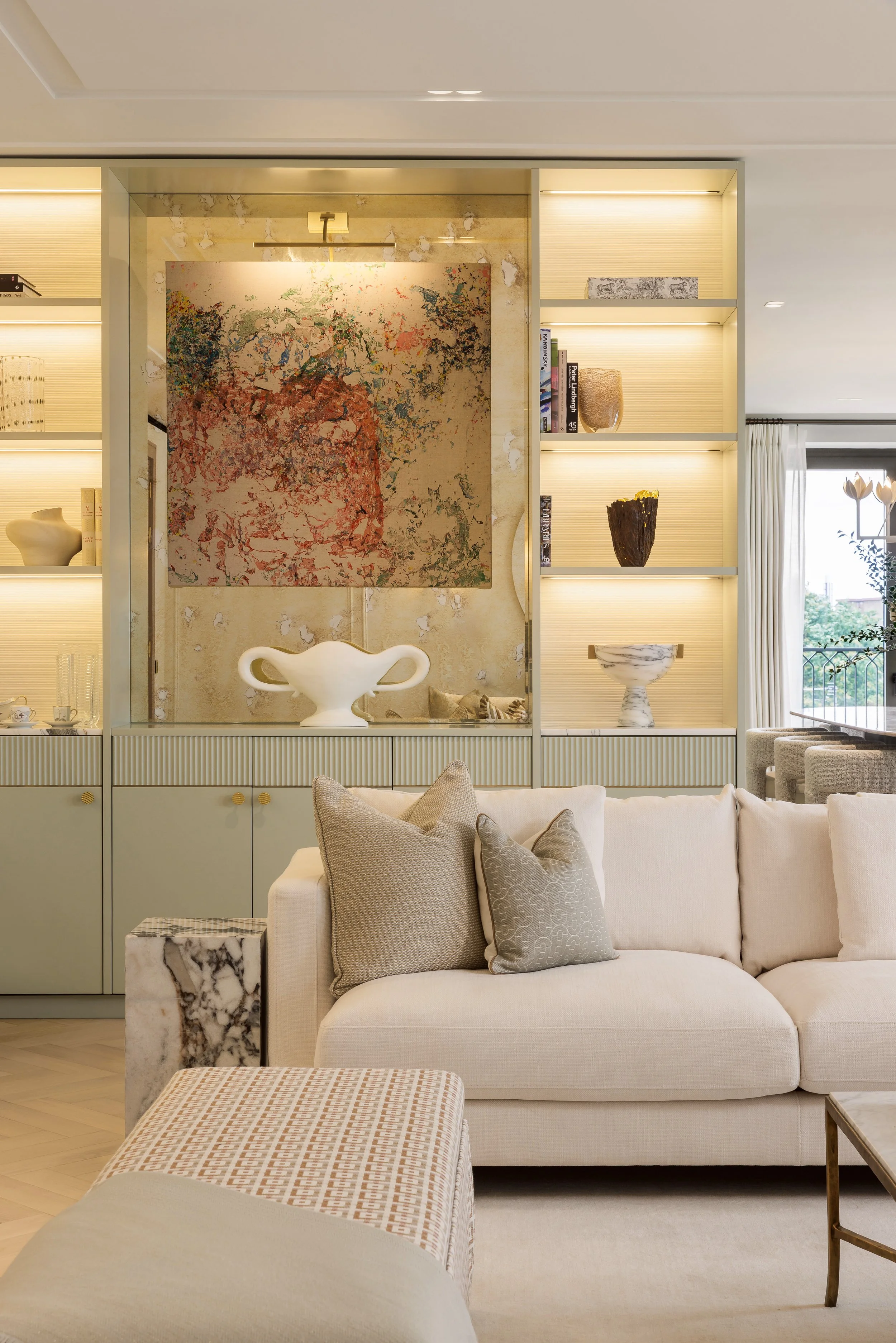 Sofa and abstract artwork framed by sage green display shelving in a four-bedroom apartment at Holland Park Gate, London