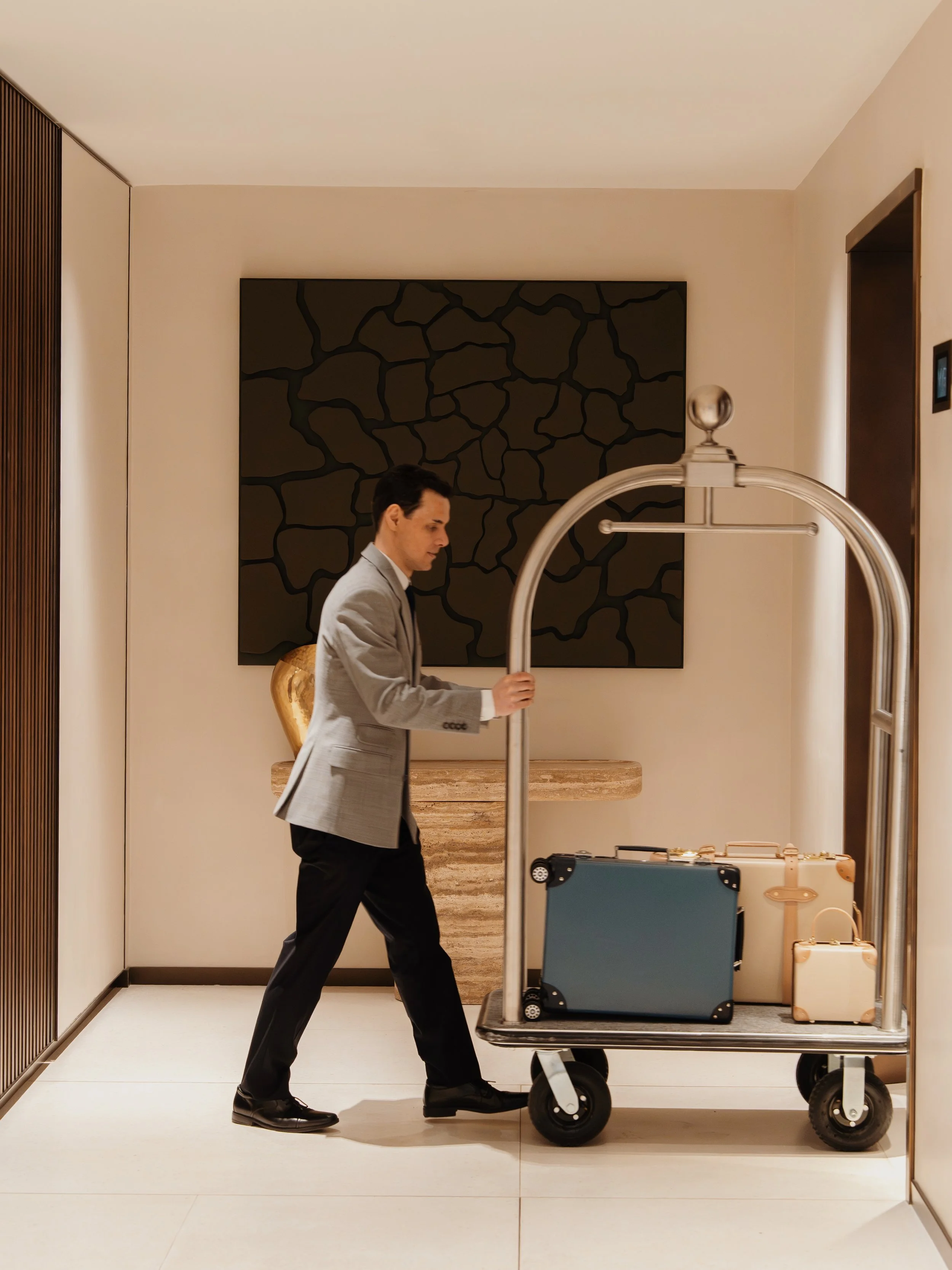 Porter wheeling Globetrotter luggage on a brass trolley through the lobby at Holland Park Gate, Kensington, London