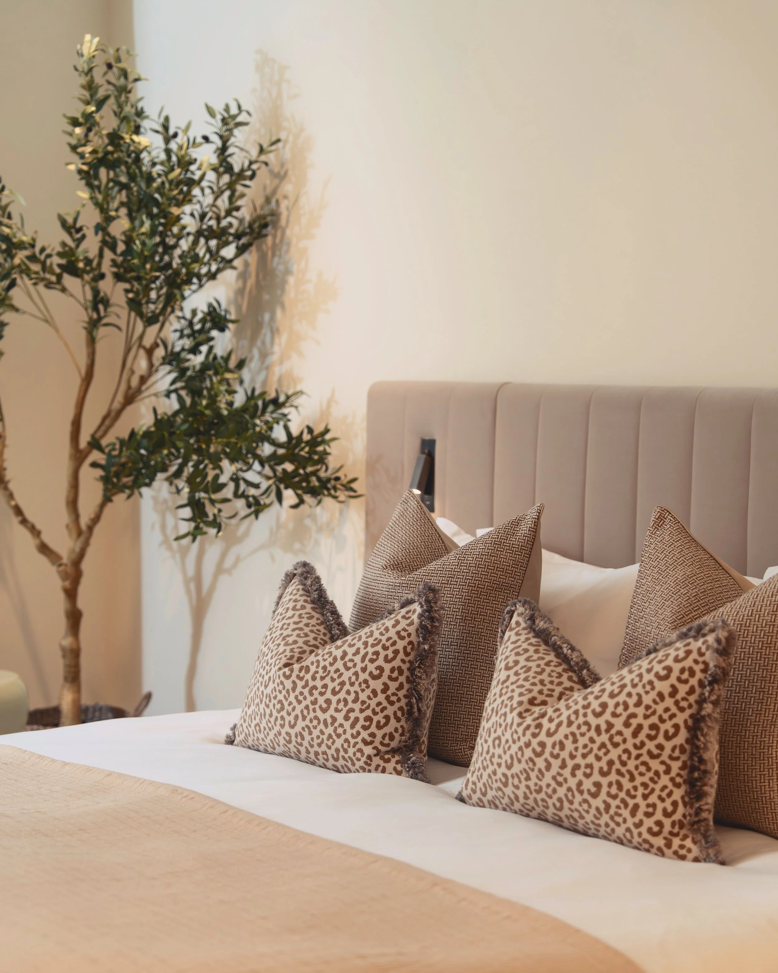 Bedroom detail with leopard print cushions, upholstered headboard and olive tree in Residence 82 at Holland Park Gate, London
