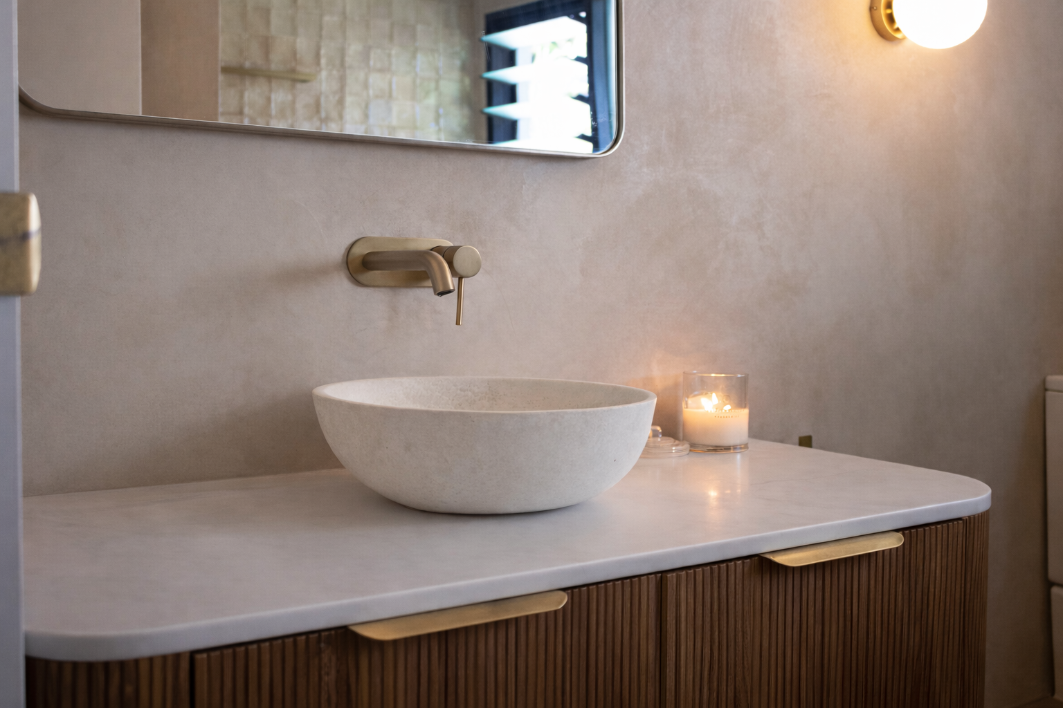 Bathroom vanity with a stone vessel sink, wall-mounted faucet, mirror, and lit candle.
