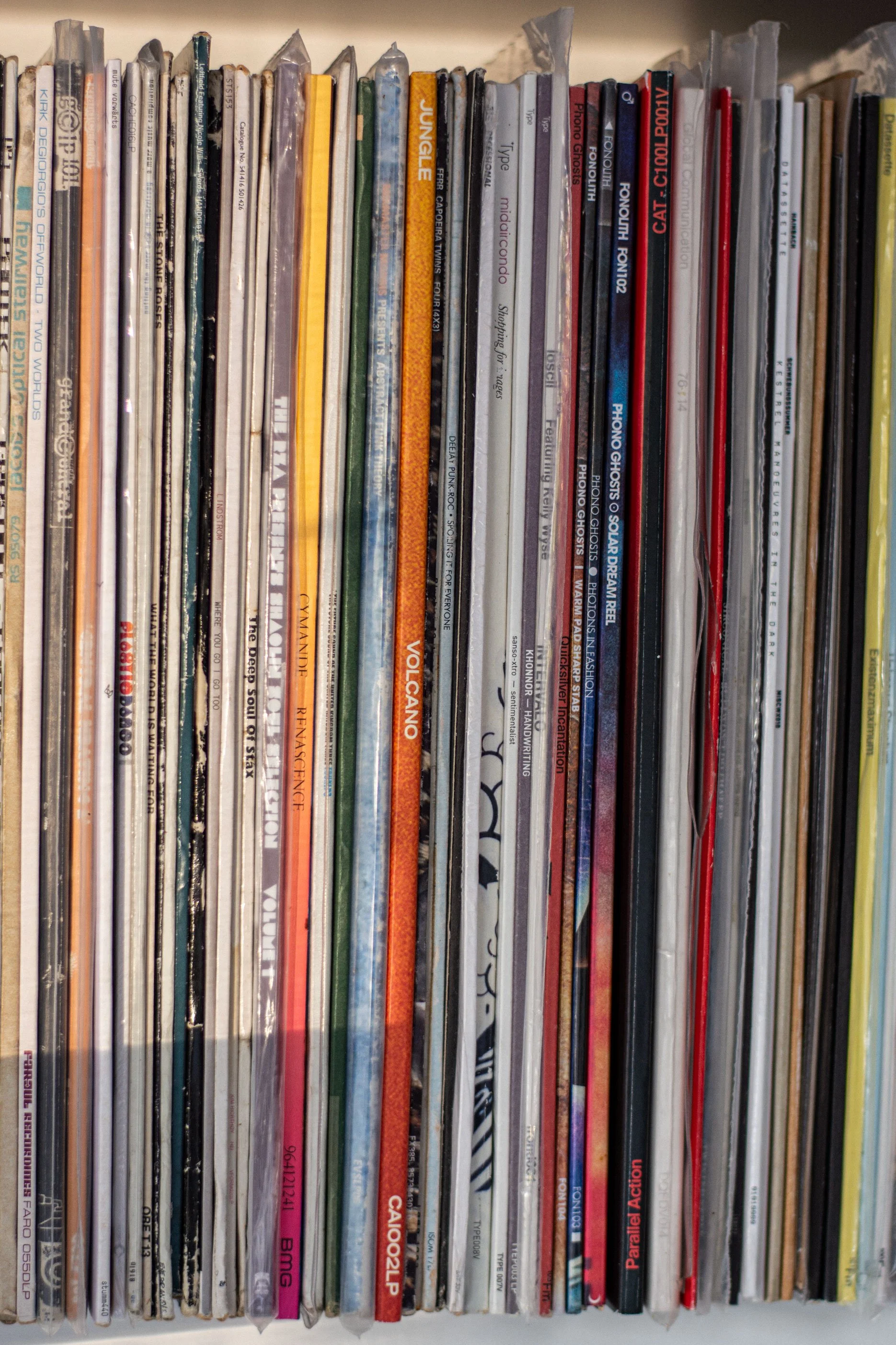 The tall and thin multicoloured stripes of the lined up spines of some of my record collection sitting on a white shelf.