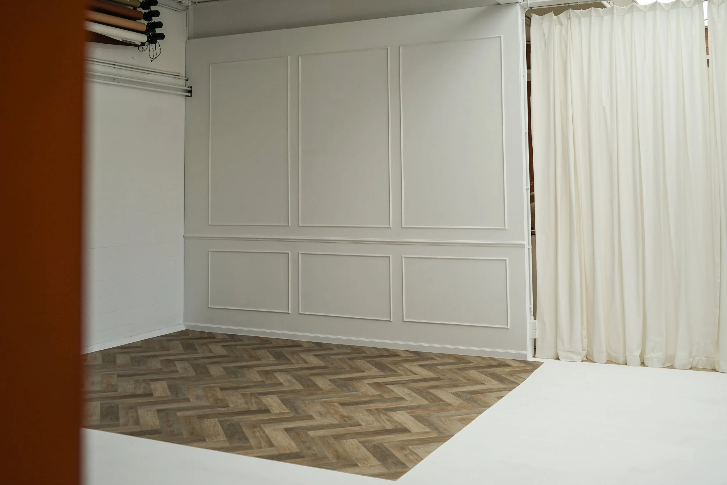 Een witte kamer met witte wandpanelen, een houten vloer en een witte gordijn aan de rechterkant.