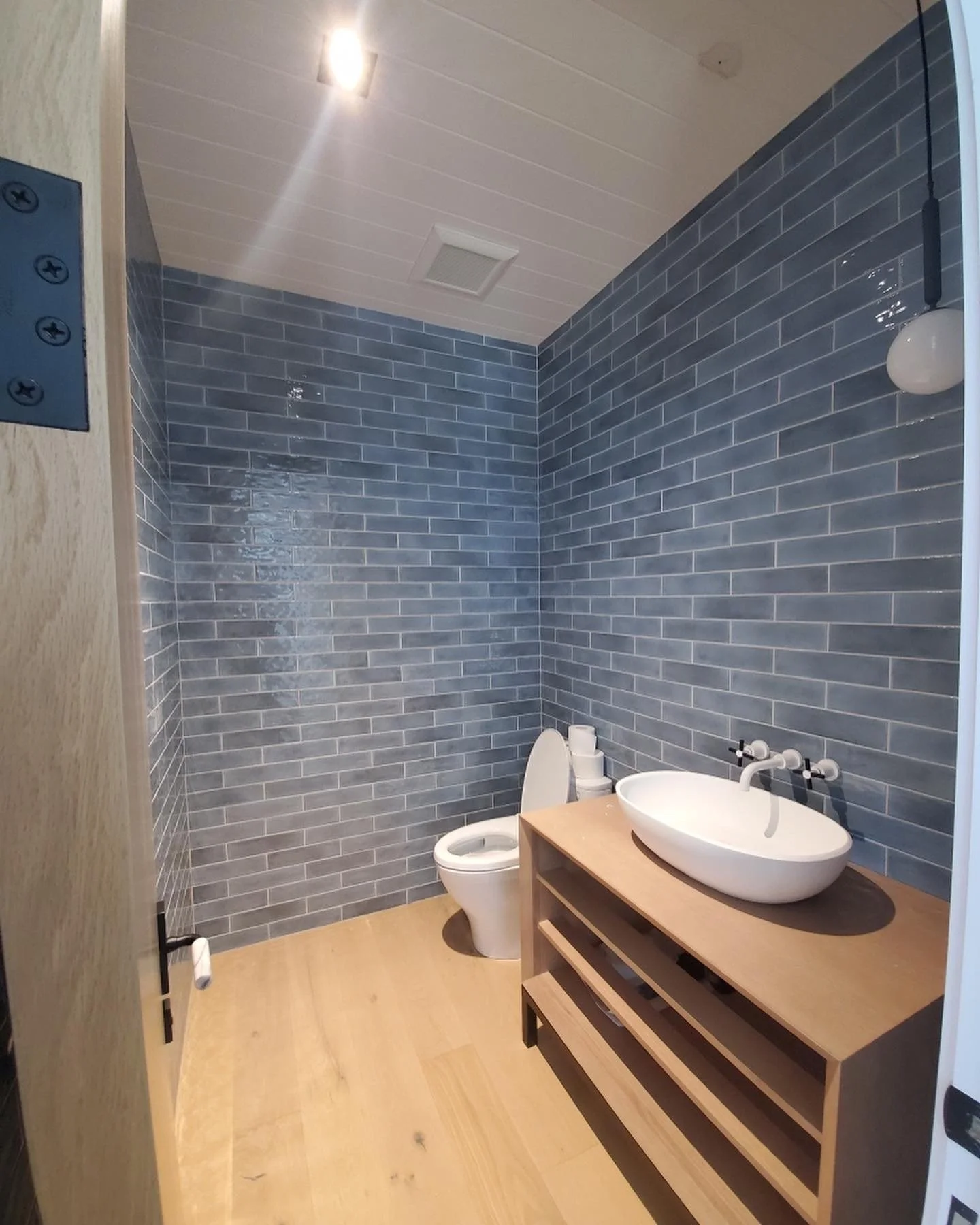 Bathroom with blue tiled walls, a white toilet, and a wooden vanity with a white oval sink and faucet.