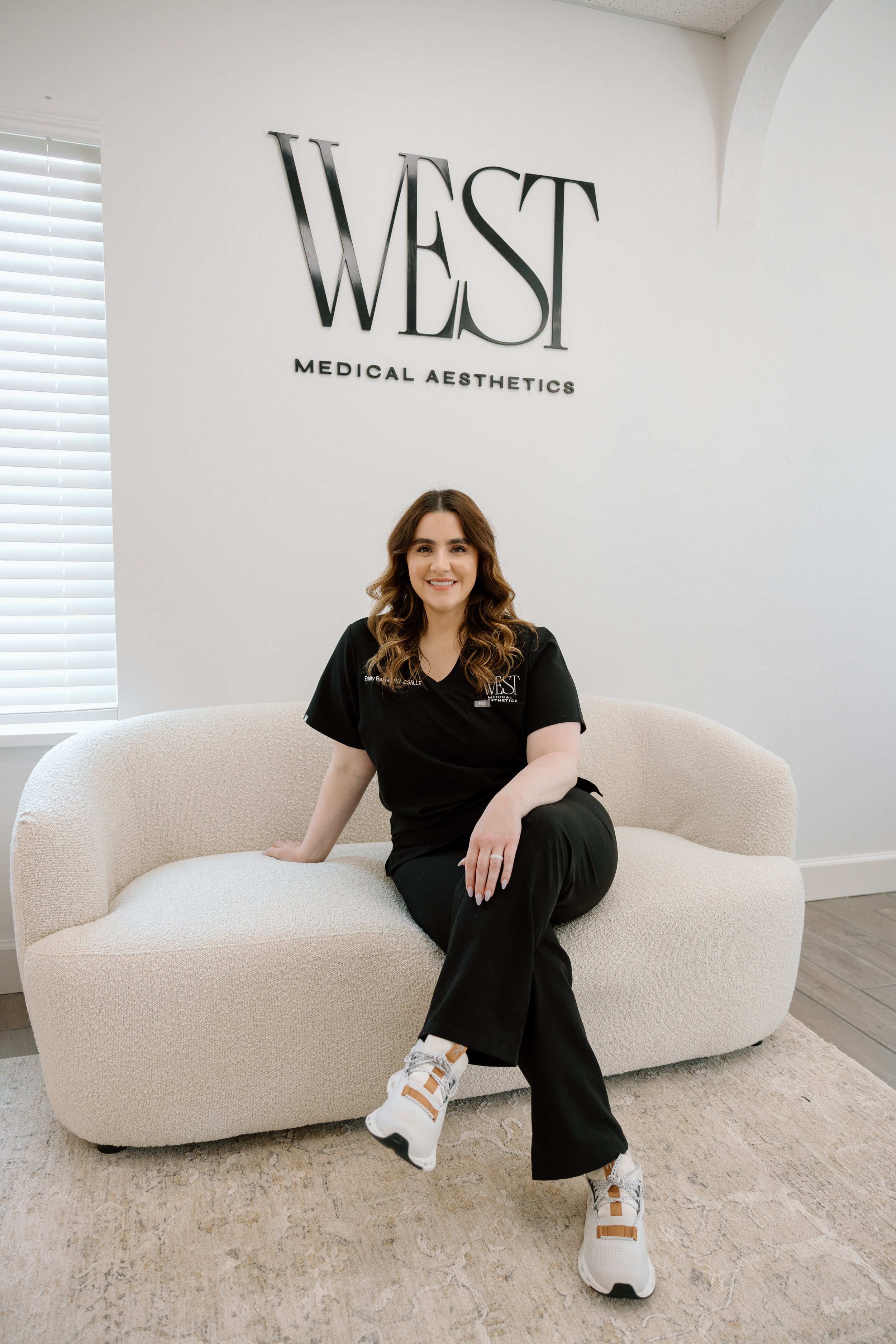 Emily Bartel, West Medical Aesthetics Founder, posing on a cream sofa for a headshot