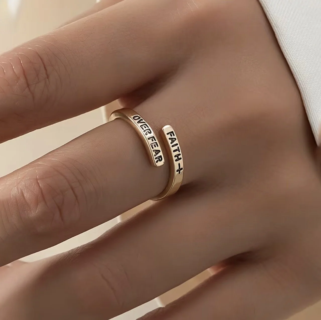 Close-up of a person's hand and waist, emphasizing both fingers with rings. The ring on the index finger reads 'FEAR', and the ring on the middle finger reads 'LOVE FEAR'. The person is wearing a white top.