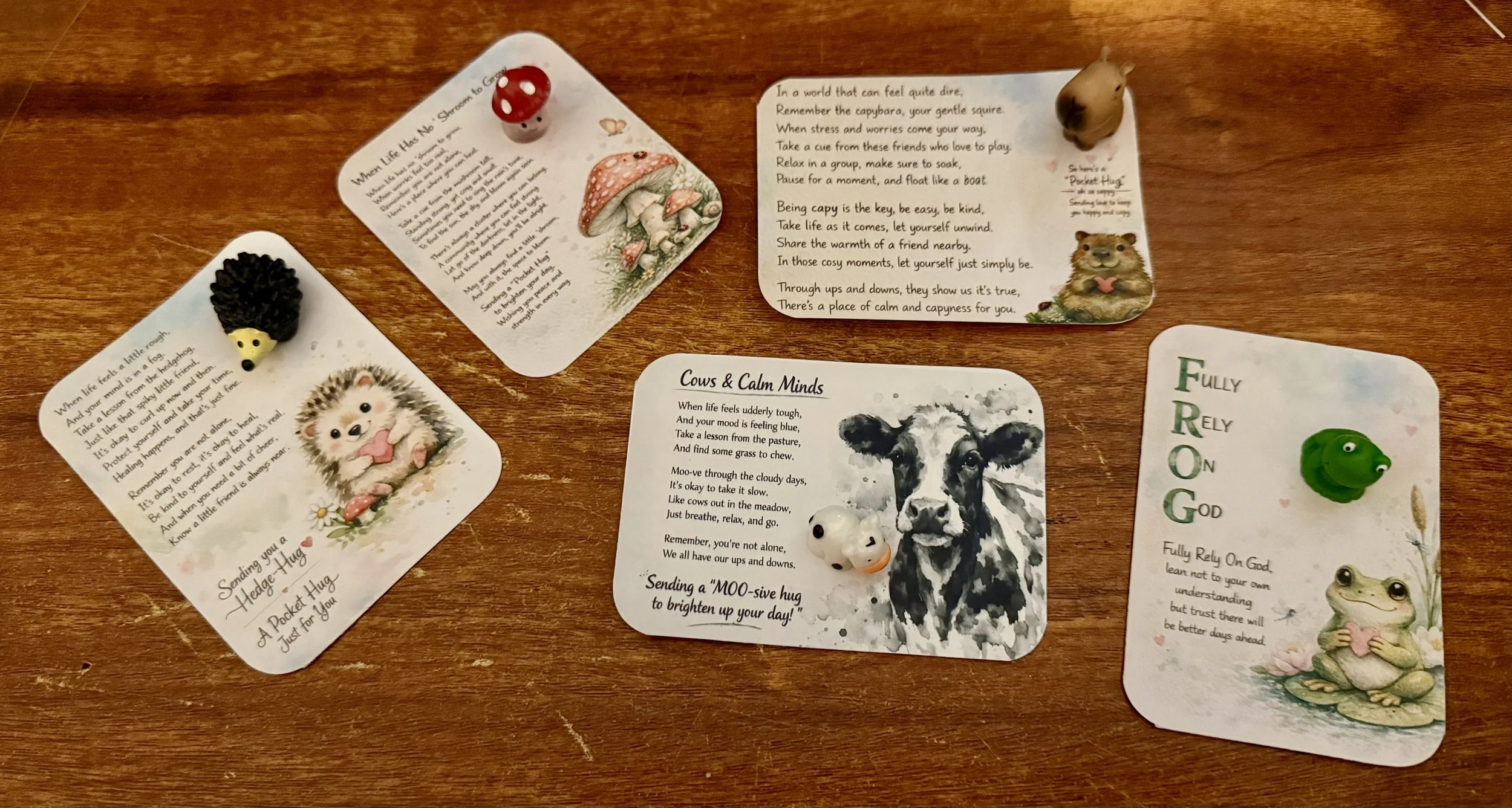 Collection of illustrated cards with nature and animal themes, decorated animals including a mushroom, hedgehog, capabara, and frog, and containing poetic texts about calmness, resilience, and friendship. Mental health