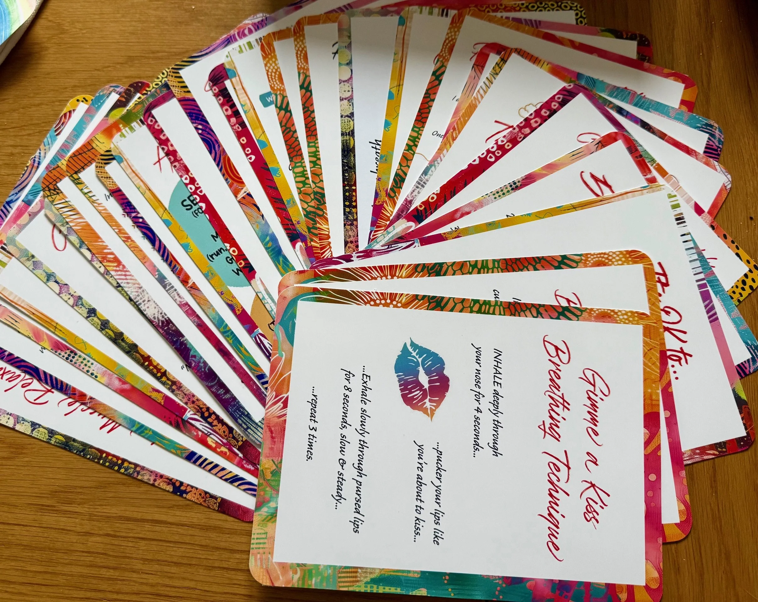 Colorful gift cards arranged in a fan shape on a wooden surface with partially visible decorative packaging in the background.