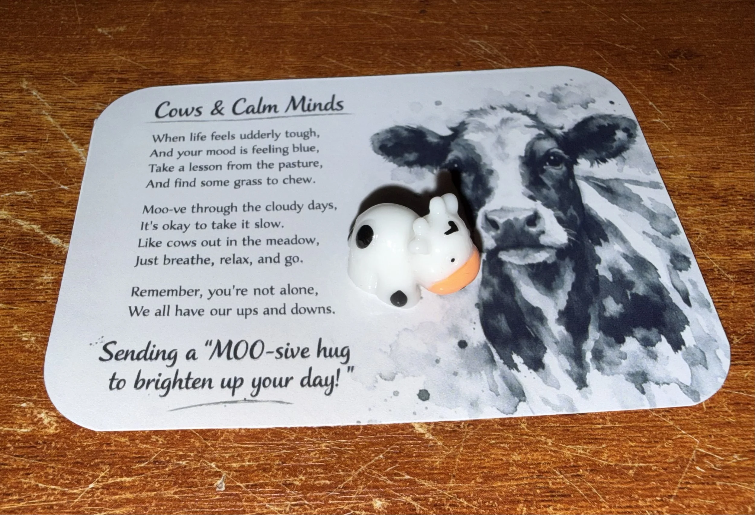 A decorative card with a black-and-white image of a cow's face, featuring large eyes and ears. The card contains a poem titled 'Cows & Calm Minds' and a small cow figurine nearby. Mental health.