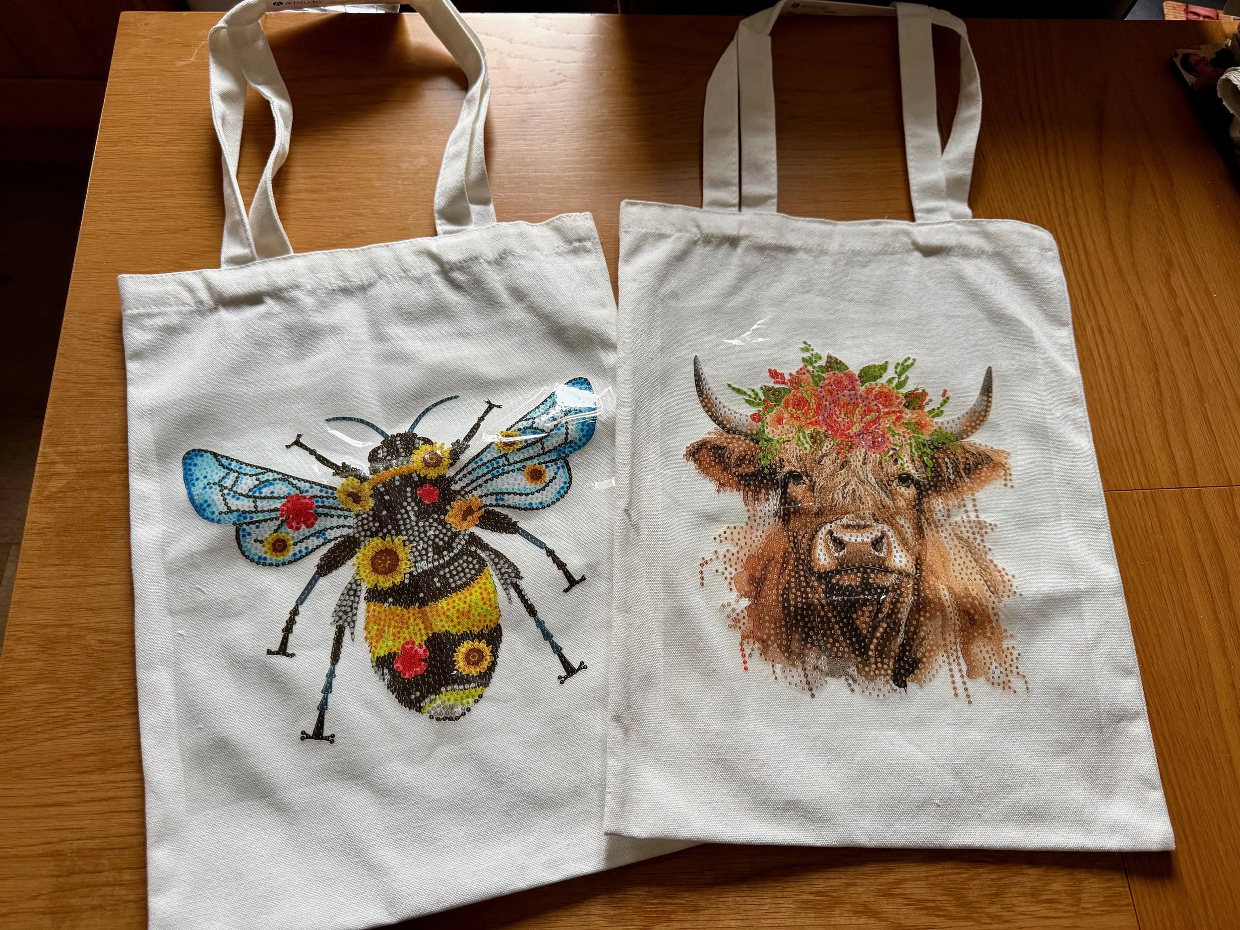Two white tote bags with colorful animal and insect designs, placed on a wooden surface.