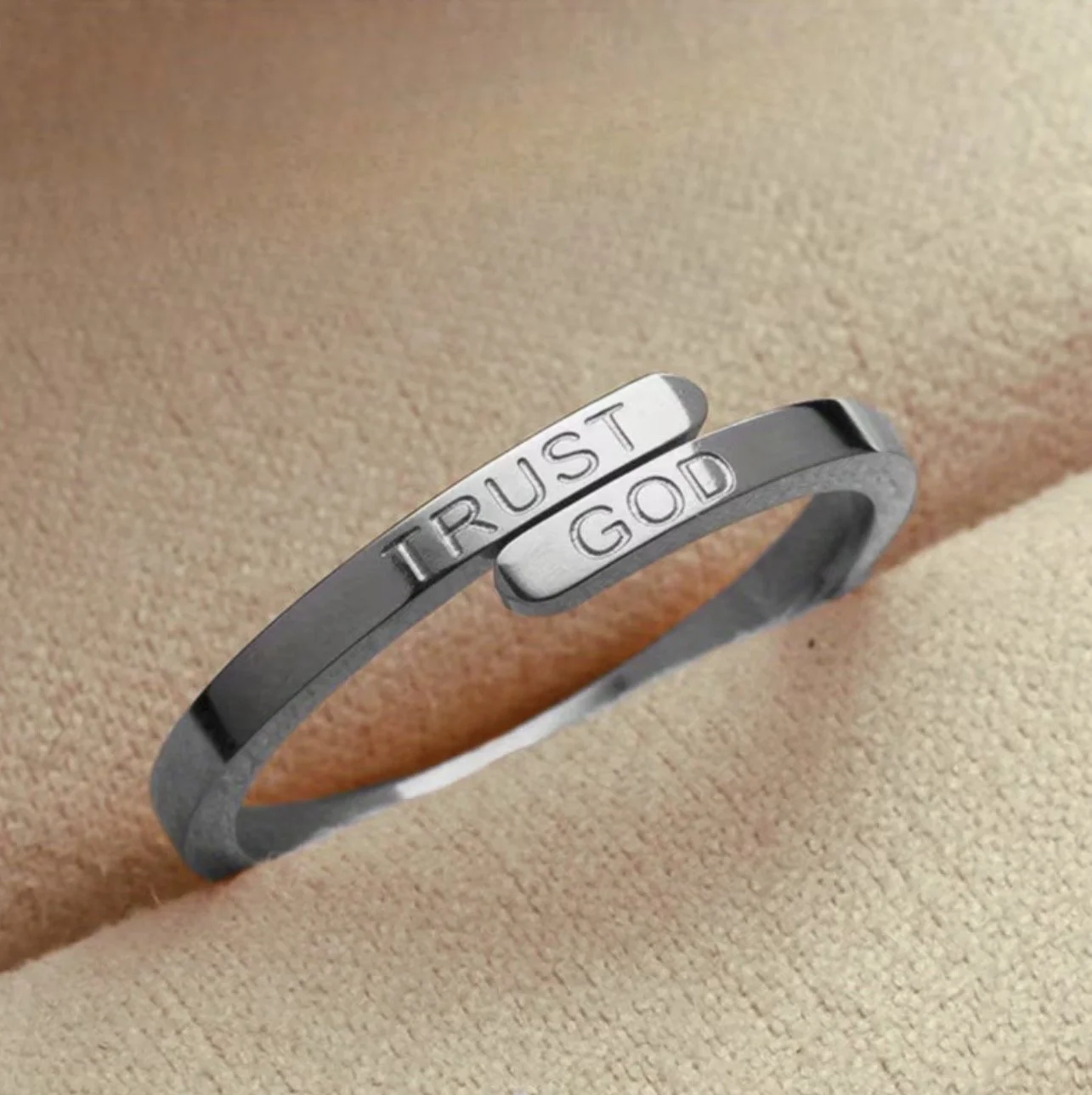 A silver bracelet with the words 'TRUST GOD' engraved on it, resting on a beige fabric background.