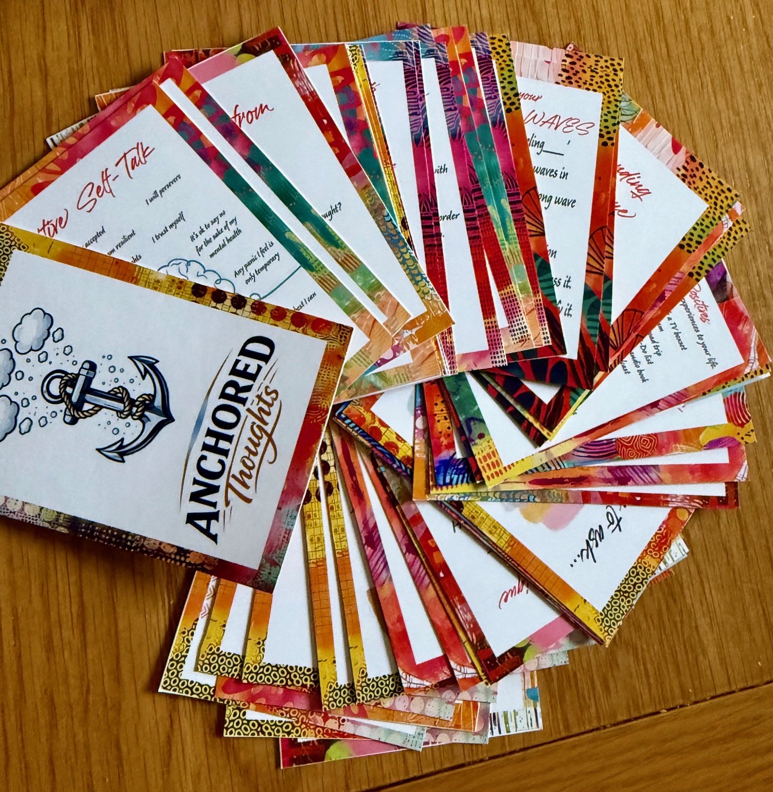 A pile of colorful, patterned paper envelopes with handwritten notes on white paper inserts, positioned on a wooden surface.
