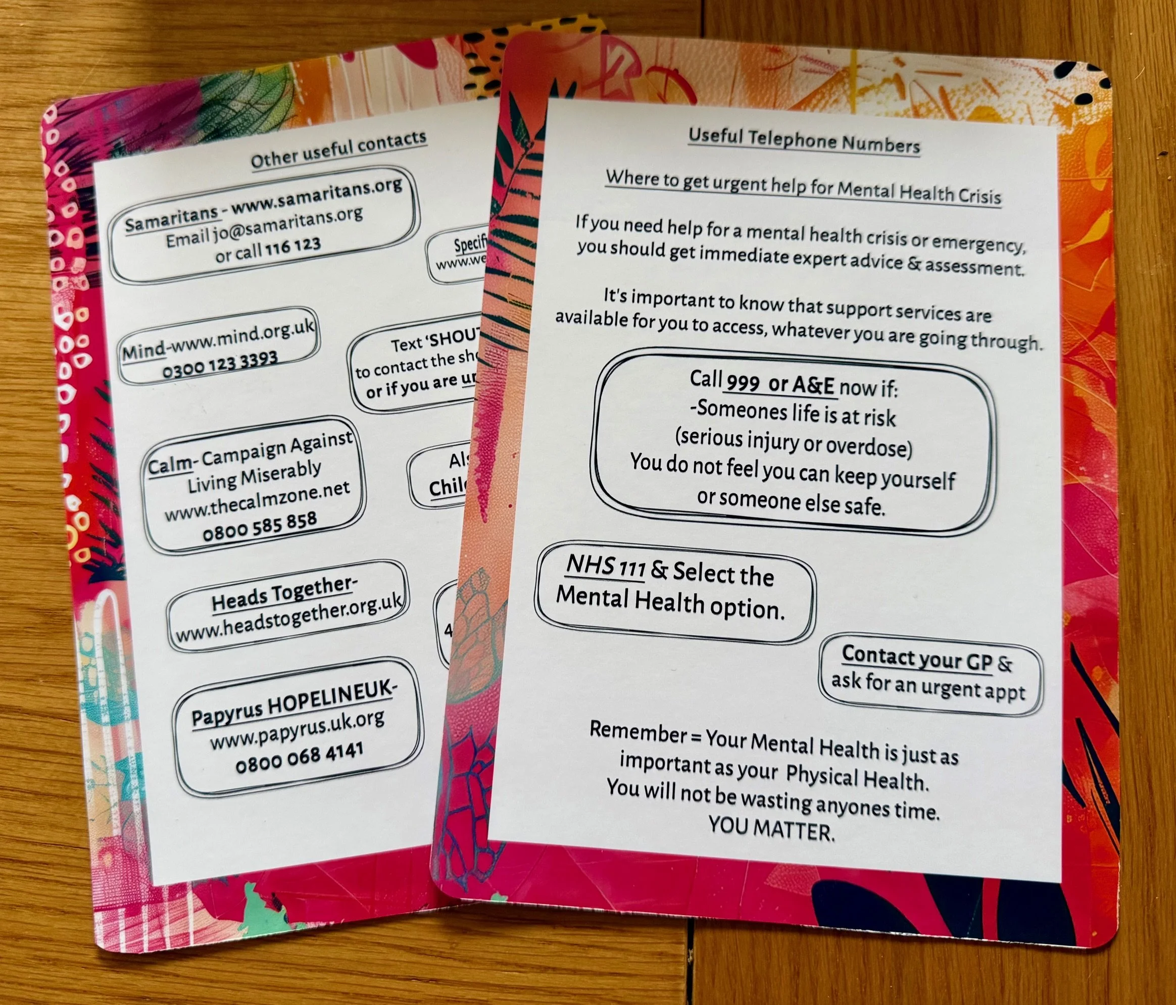 Multiple colorful pamphlets with mental health and emergency contact information on a wooden surface.