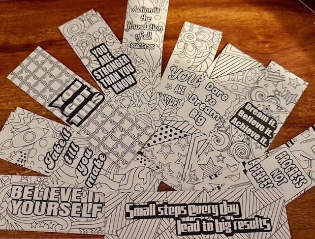 Collection of colouring bookmarks with motivational quotes and patterns spread on a wooden surface. mental health