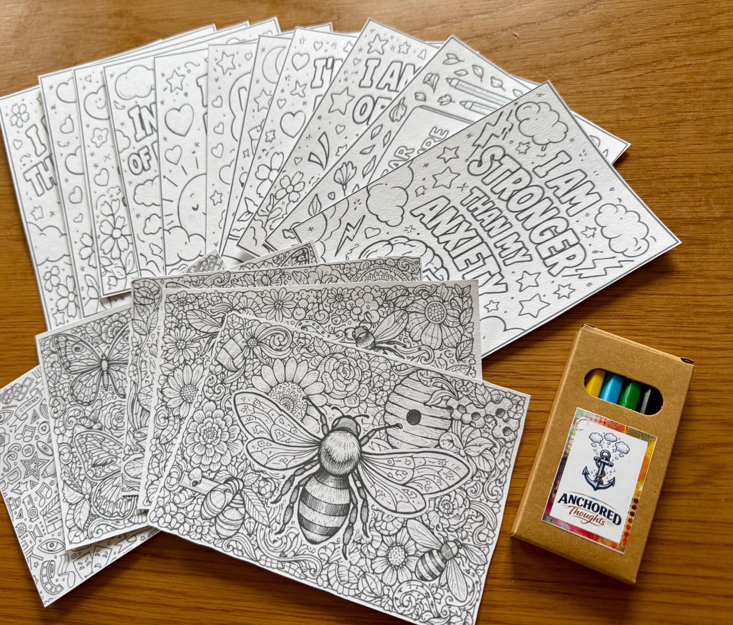 Coloring pages spread out on a wooden surface, with a box of colored pencils nearby.