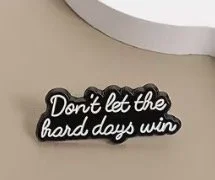 A pin badge with the quote 'Don't let the hard days win' in white script on a black background. Mental Health (Anchored Thoughts)
