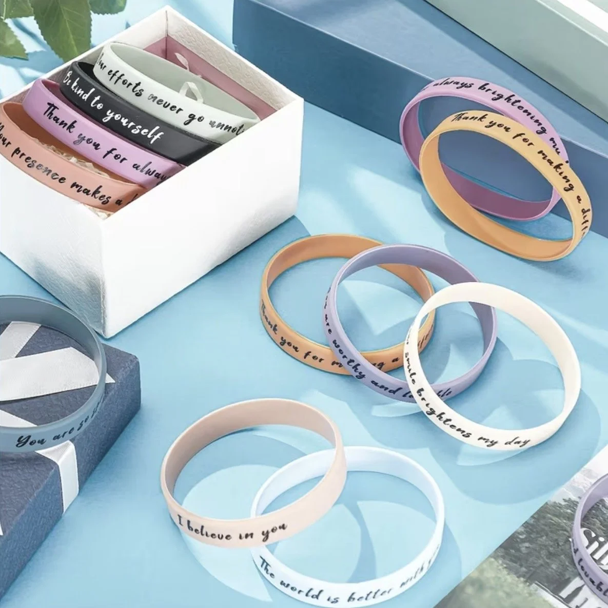 Colorful silicone wristbands with inspirational messages laid on a blue surface and in a white box.