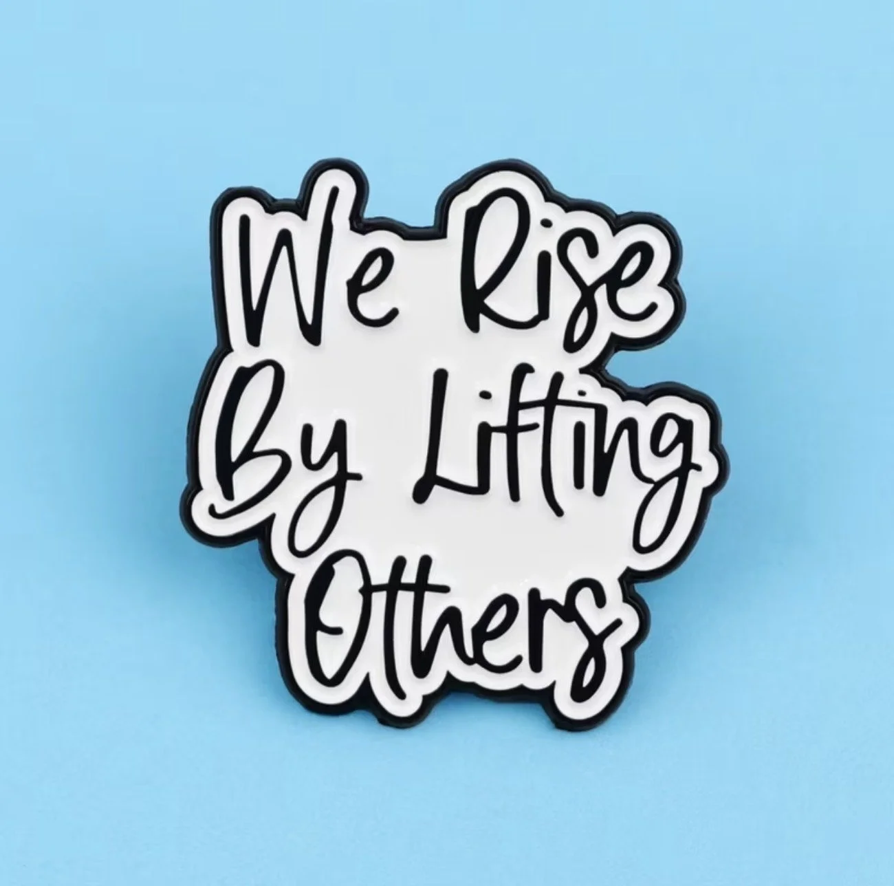 Sticker with the text "We Rise by Lifting Others" in black cursive letters on a white background, outlined in black, Mental Health (Anchored Thoughts)