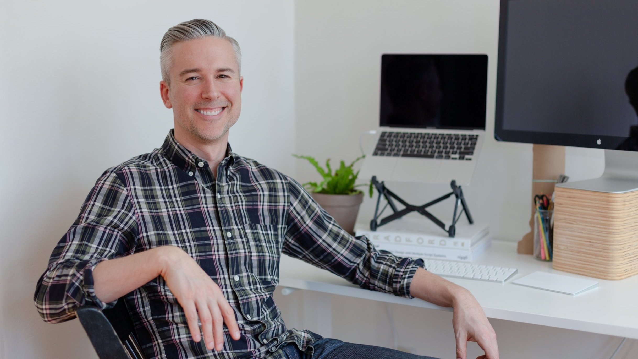 Ben Spear sitting at a computer work desk, turning to the camera and smiling.