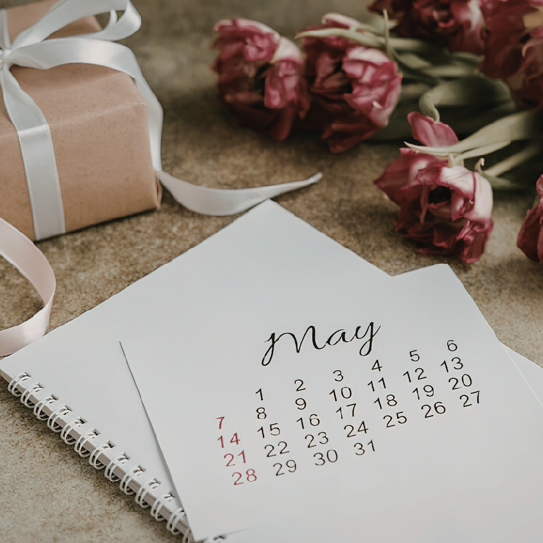 May calendar page next to a gift box and pink tulips, representing the step to secure a wedding or event date with Breemar Flower Farm, an Ashland farmer-florist in Virginia.