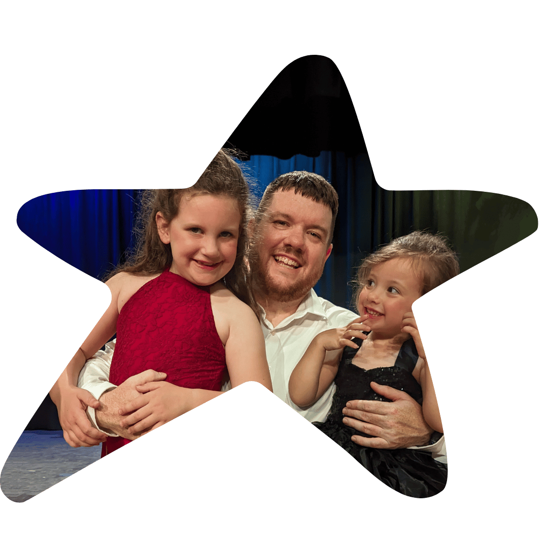 A man with two young girls smiling, with a dark background and blue curtains.