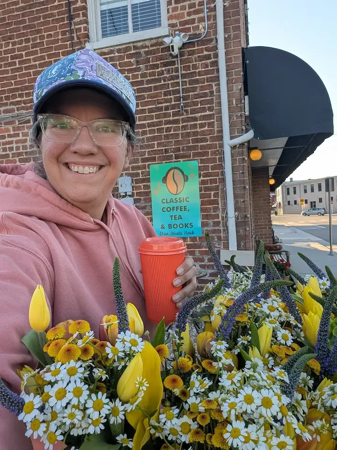 Nicole Dillon of Breemar Flower Farm holding a bouquet of yellow flowers and a coffee cup outside a local coffee shop in Ashland, VA