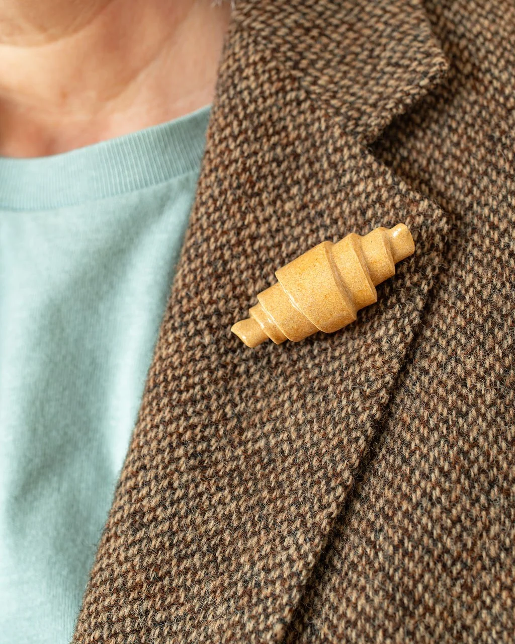 Hand holding a card with a ceramic pastry fridge magnet shaped like a glazed stoneware croissant.
