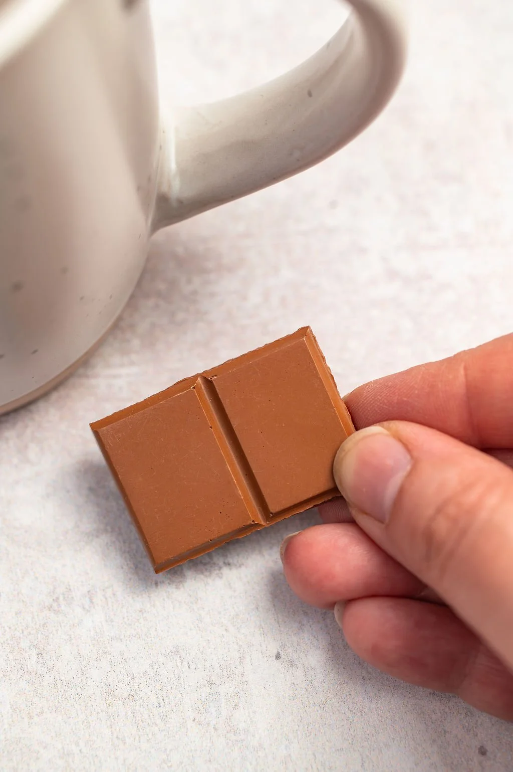 A hand holding a card with a small chocolate pin badge on it, labeled "Chocolate Pin Badge" and made with Jesmonite.