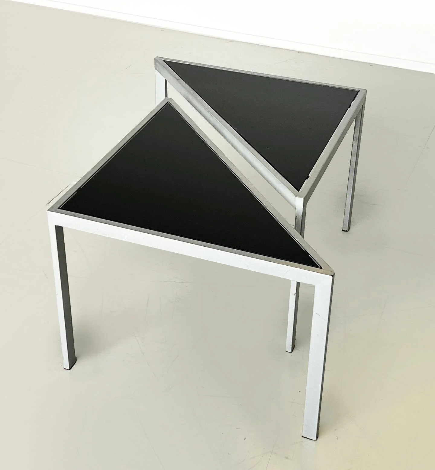 New: A striking pair of triangular geometric side tables with inset black glass and slim metal frames. Their modular design allows them to be styled together as a sculptural composition or used separately. Minimal yet bold, they bring a geometric edg