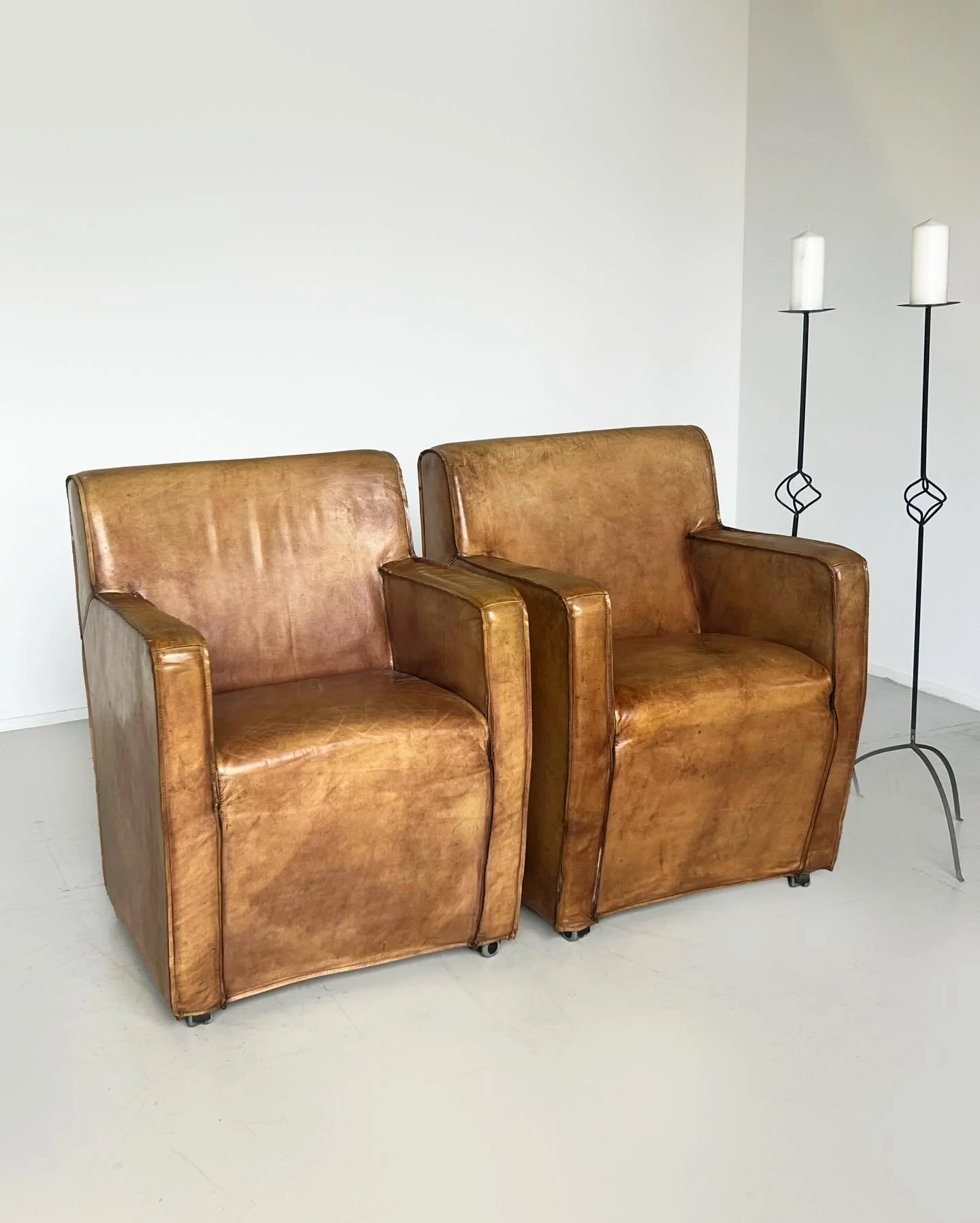 New: A beautifully worn pair of leather armchairs with a rich, lived-in tonal variation, giving each chair a warm, character-filled presence. Their boxy yet compact silhouette and offer a grounded, architectural feel, while the subtle distressing add