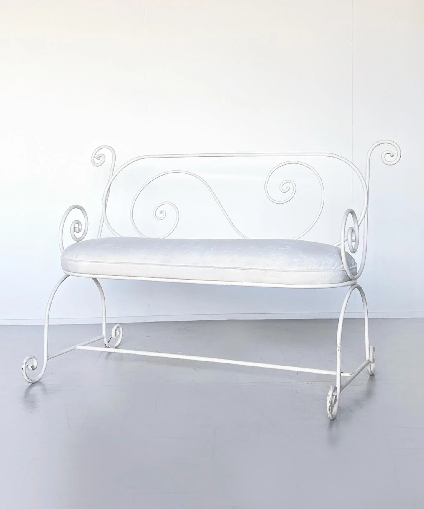 Sold: A refined French bench with a slender iron frame shaped into fluid, continuous scrolls. Its minimalist silhouette is softened by a tailored upholstered seat, creating a piece that feels delicately sculptural. Ideal for adding a touch of softnes