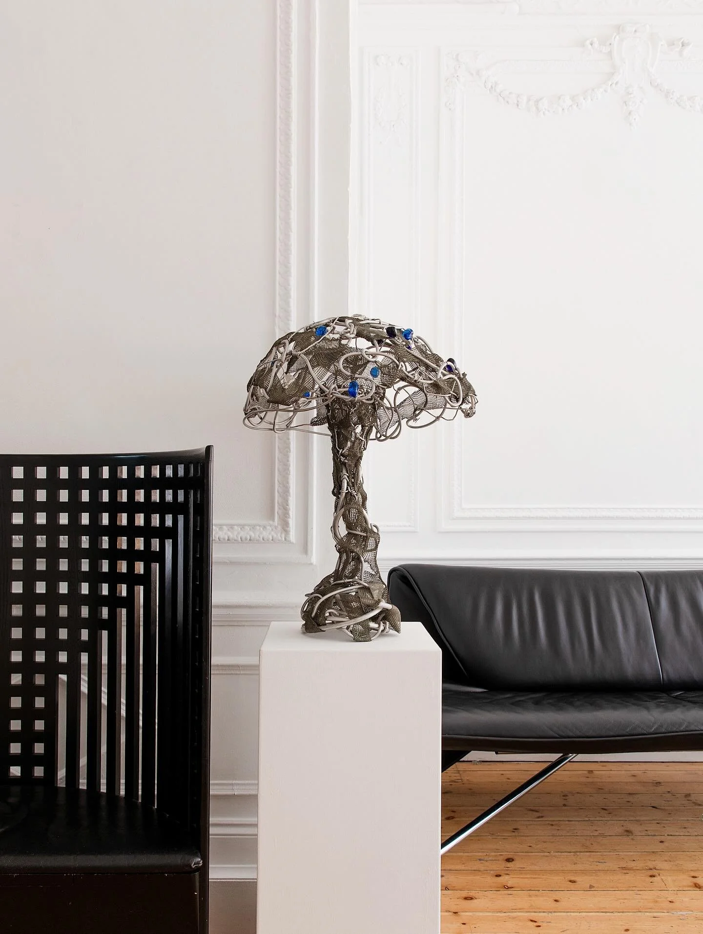 An avant-garde jewelled sculptural lamp composed of interwoven metal mesh and looping aluminium wire, forming an organic, almost mycelial silhouette. Electric blue glass jewels punctuate the structure, giving it a kinetic, experimental presence. More