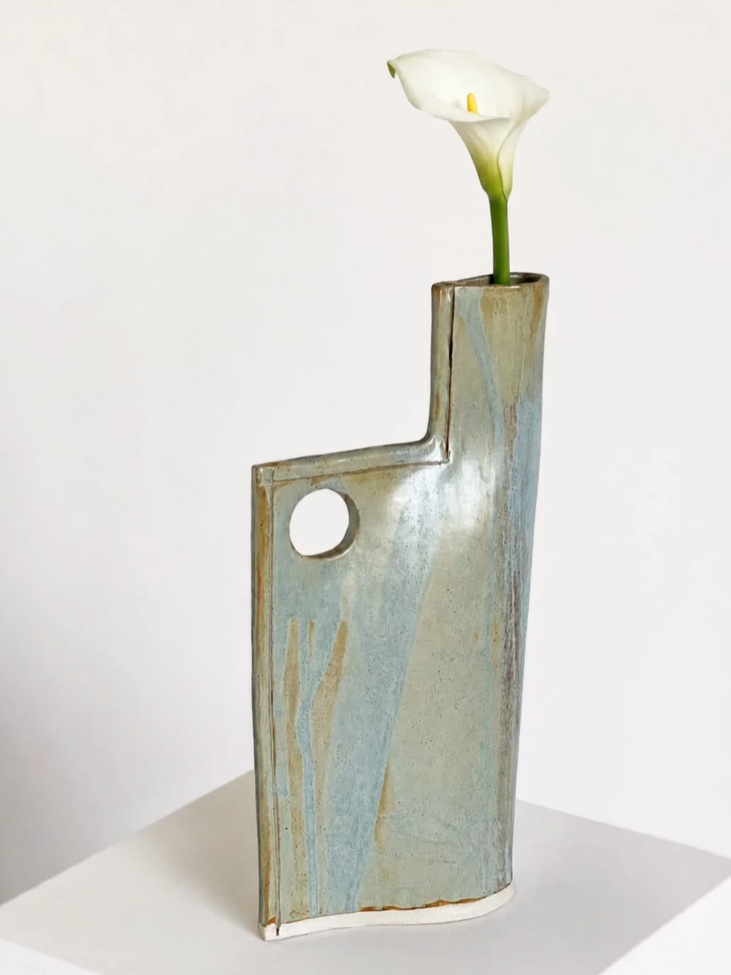 Now Sold: Geometric single stem flower vase, both functional sculpturally and as a vase. Variations of neutral greens and blues in tone, hint to brutalist form with circular cut out. Formed from a single folded ceramic, an elegant slender overall for